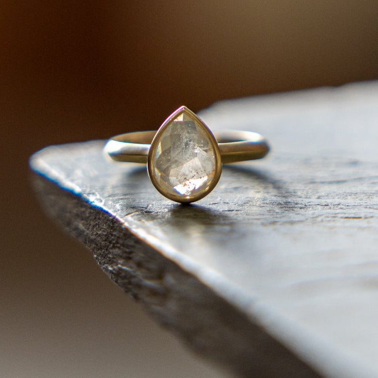 Gold ring with a pear-shaped rose cut diamond on a wooden surface with a blurred background